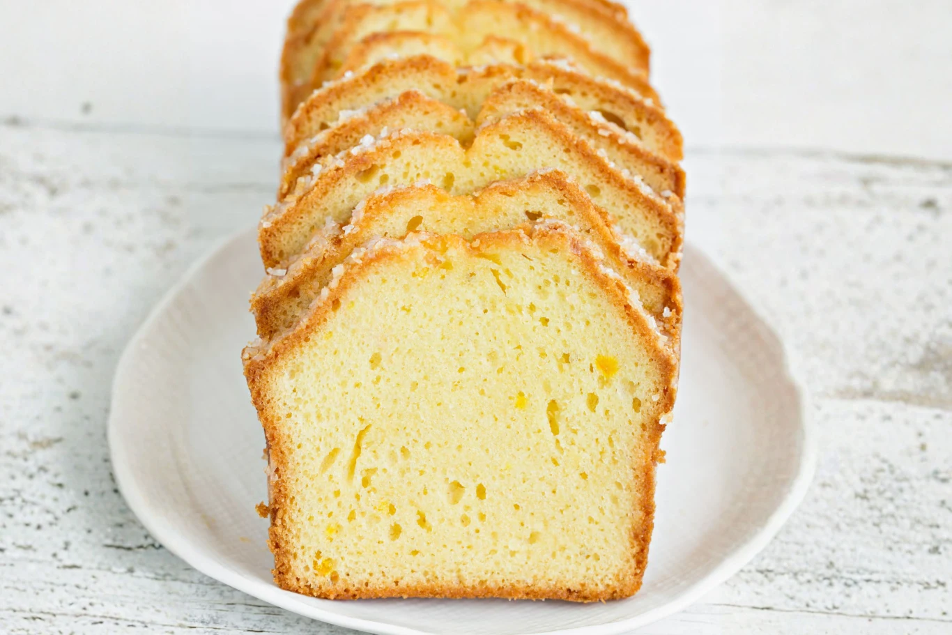 Pokrojona babka piaskowa o złocistej, delikatnie wilgotnej strukturze, ułożona w rzędu na białym talerzu na jasnym tle.