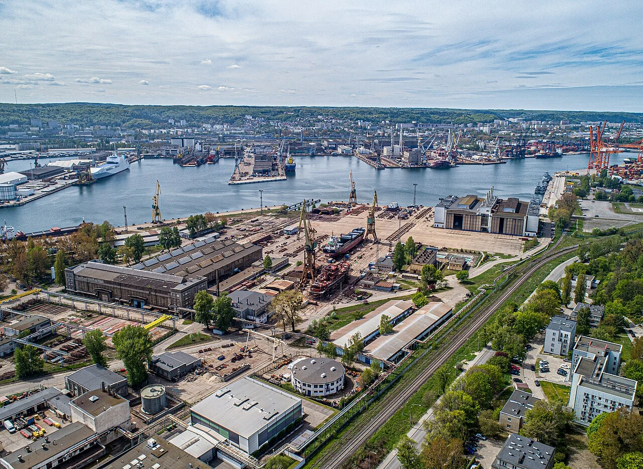 PGZ Stocznia Wojenna zajmie się m.in. testami maszyn Widok na rozległą stocznię PGZ Stoczni Wojennej z dźwigami, okrętami, halami oraz liniami kolejowymi przy rzece.