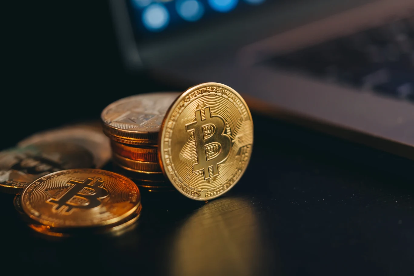 Kryptowaluty ma w swoich kieszeniach ok. 2,7 mln dorosłych Polaków Złota moneta z symbolem bitcoina na tle innych monet i fragmentu laptopa, kontekst kryptowalut w Polsce