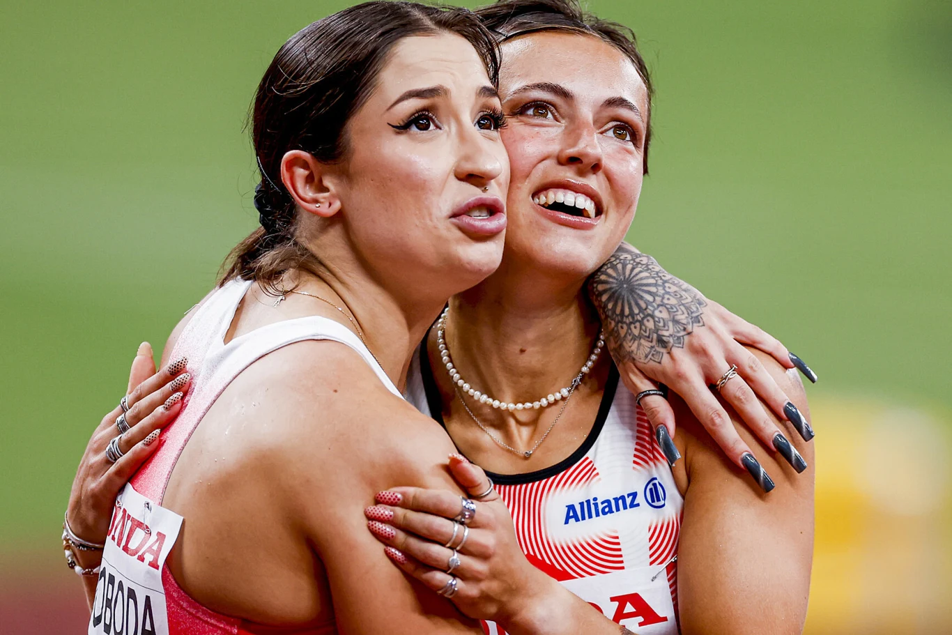 Dwie zawodniczki w sportowych strojach obejmują się, wyrażając silne emocje po zakończonych zawodach, jedna z nich ma ozdobne wzory na paznokciach i tatuaż na dłoni.