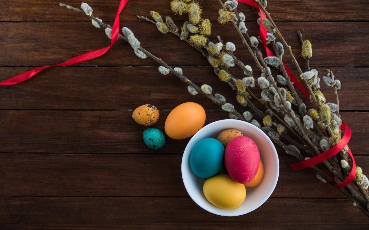 Zwyczaje i przesądy związane z Poniedziałkiem Wielkanocnym Kolorowe pisanki w misce i bazie z czerwoną wstążką na drewnianym stole, zwyczaje wielkanocne.