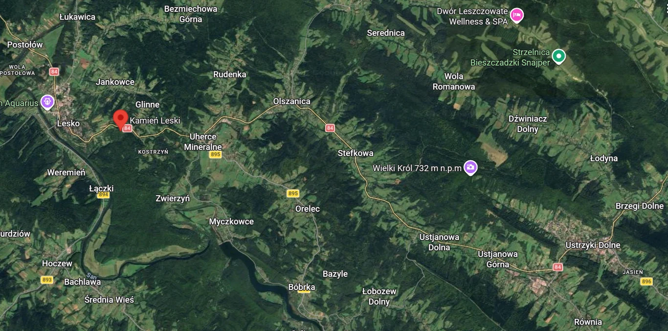 Kamień Leski leży przy drodze 84 w kierunku na Ustrzyki Dolne. fragment mapy satelitarnej południowo-wschodniej Polski z wyraźnie oznaczonymi miejscowościami, regionami leśnymi i punktami orientacyjnymi takimi jak Lesko, Ustrzyki Dolne, Wielki Król oraz ikony lokalizacji usług wypoczynkowych