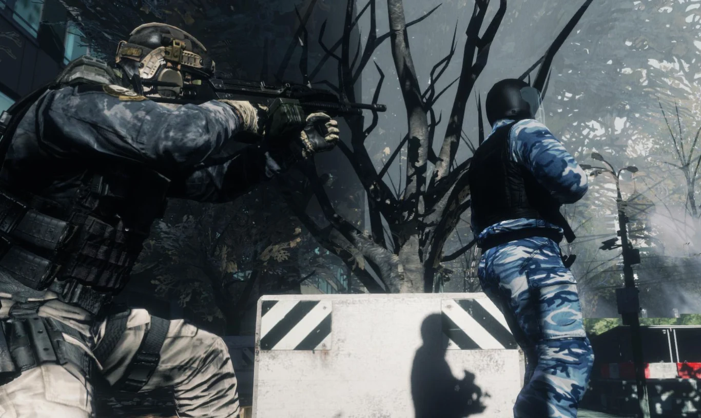 Dwóch uzbrojonych żołnierzy w kamuflażu i opancerzeniu jest gotowych do walki za betonową osłoną, jeden celuje z karabinu, drugi obserwuje otoczenie; w tle widać nagie, poskręcane drzewa oraz fragment ulicy.
