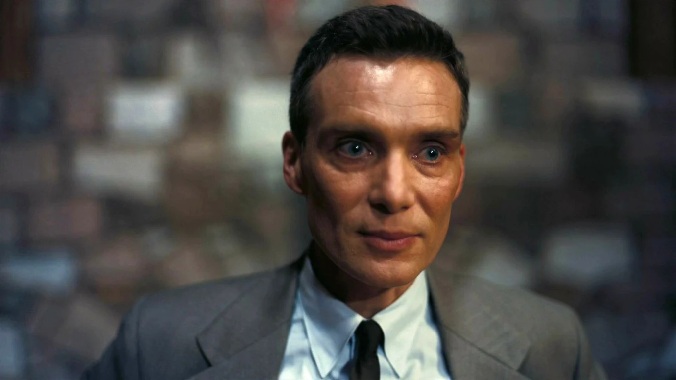 Cillian Murphy w filmie "Oppenheimer" Cillian Murphy jako Oppenheimer w szarym garniturze i białej koszuli, na tle rozmytych kształtów.