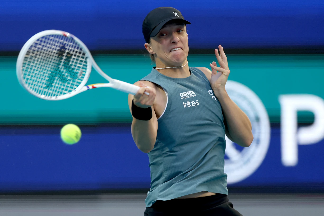 tenisistka podczas dynamicznego uderzenia forehandem, skupiona na piłce lecącej w jej kierunku, ubrana w sportowy strój i czapkę, z widoczną energią i determinacją w grze