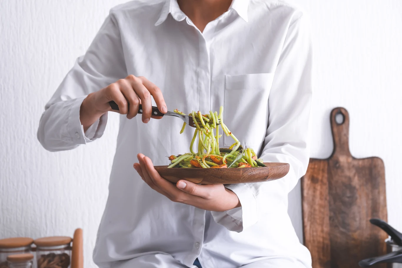 Czego warto użyć do zrobienia obiadu? Ten produkt ma wiele cennych właściwości Osoba w białej koszuli miesza makaron z pesto i warzywami w drewnianej misce, używając widelca.
