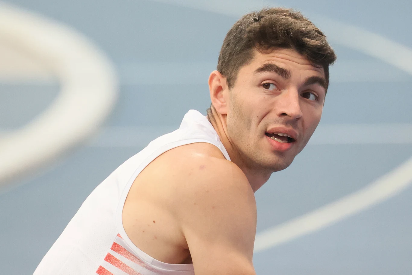 młody mężczyzna w sportowej koszulce na bieżni lekkoatletycznej, odwrócony w bok z lekko otwartymi ustami i skupionym wyrazem twarzy