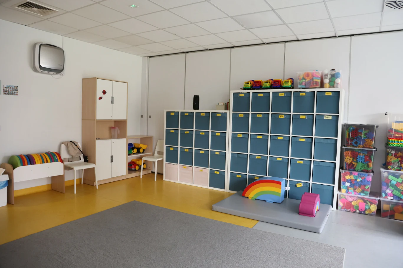 Logopedzi pracują m.in. w przedszkolach. Sala przedszkolna z kolorowymi szafkami, półkami pełnymi zabawek i akcesoriami oraz miękkimi elementami do zabawy.