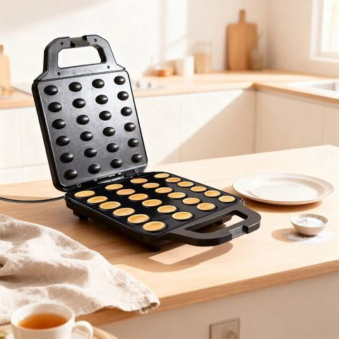 Otwarta gofrownica zapełniona równomiernie piekącymi się mini ciasteczkami ustawiona na jasnym, drewnianym blacie w kuchni; obok pusta biała porcelanowa miska, talerz oraz niewielka miseczka z cukrem.