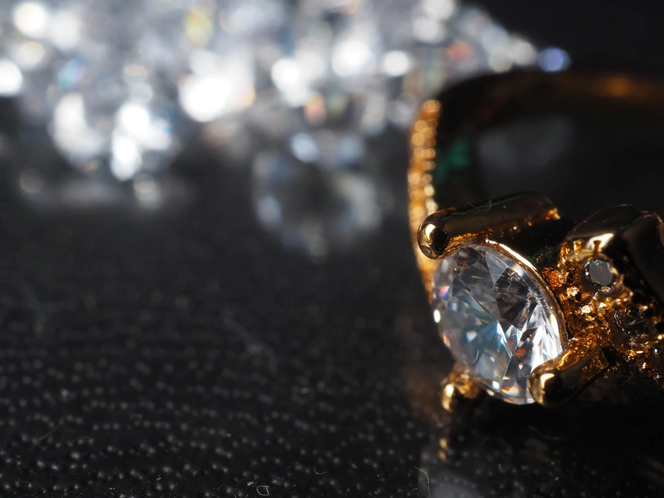 Złoty pierścionek z dużym, szlifowanym diamentem w centrum, z detalami jubilerskimi na oprawie, sfotografowany z bliska na ciemnym tle, w tle rozmyte refleksy świetlne odbijające się od innych diamentów.