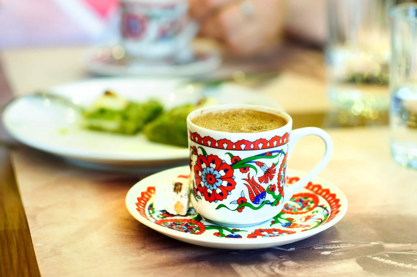 Zwykła kawa to za mało? Wersja z matchą zapewni większą energię. Filiżanka kawy w ozdobnej porcelanie na spodeczku, nawiązanie do napoju z matchą.