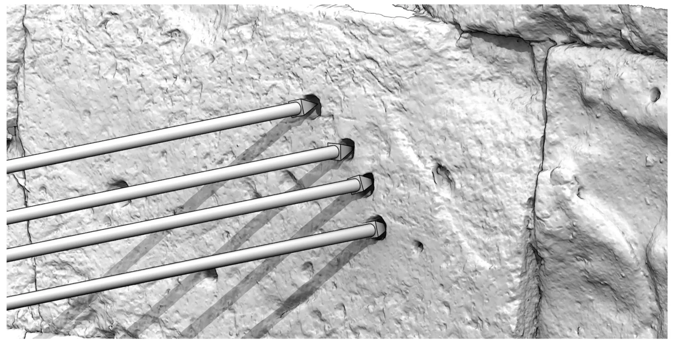 Cztery metalowe pręty zamocowane równolegle w szorstkiej, płaskiej powierzchni betonowej z widocznymi zaciekami i pęknięciami w strukturze betonu.