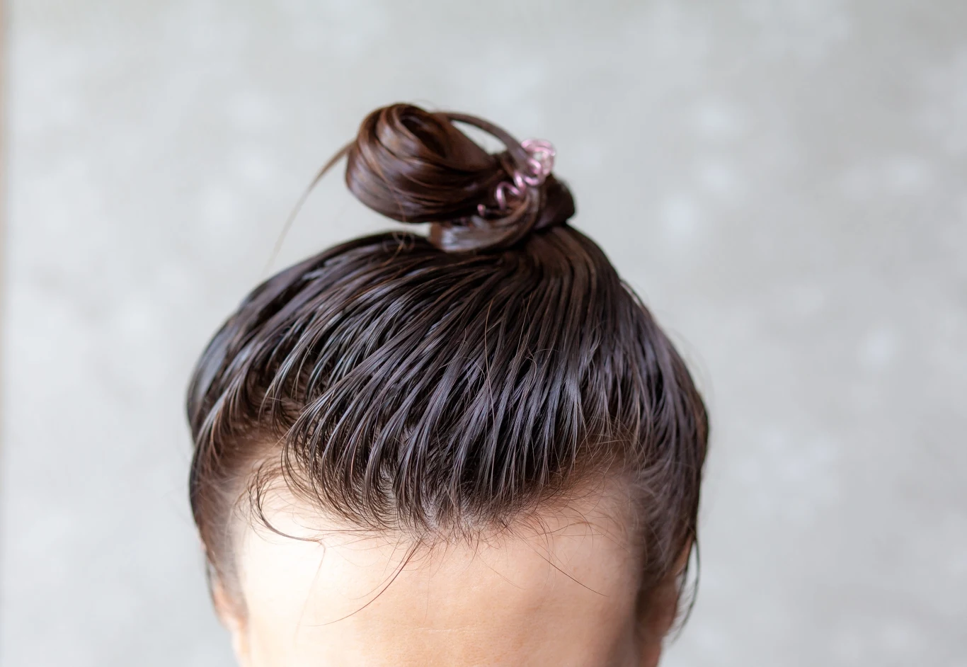 ciemne, świeżo umyte włosy upięte w mały koczek na czubku głowy, związane plastikową gumką
