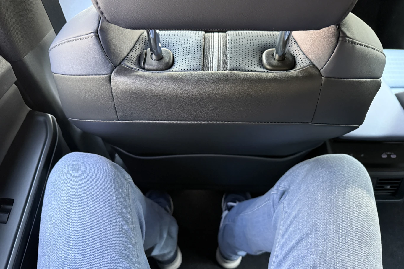 nogi ubrane w jasnoniebieskie spodnie dżinsowe ustawione naprzeciw tylnej części przedniego fotela samochodu, niewielka ilość wolnej przestrzeni między kolanami a oparciem fotela