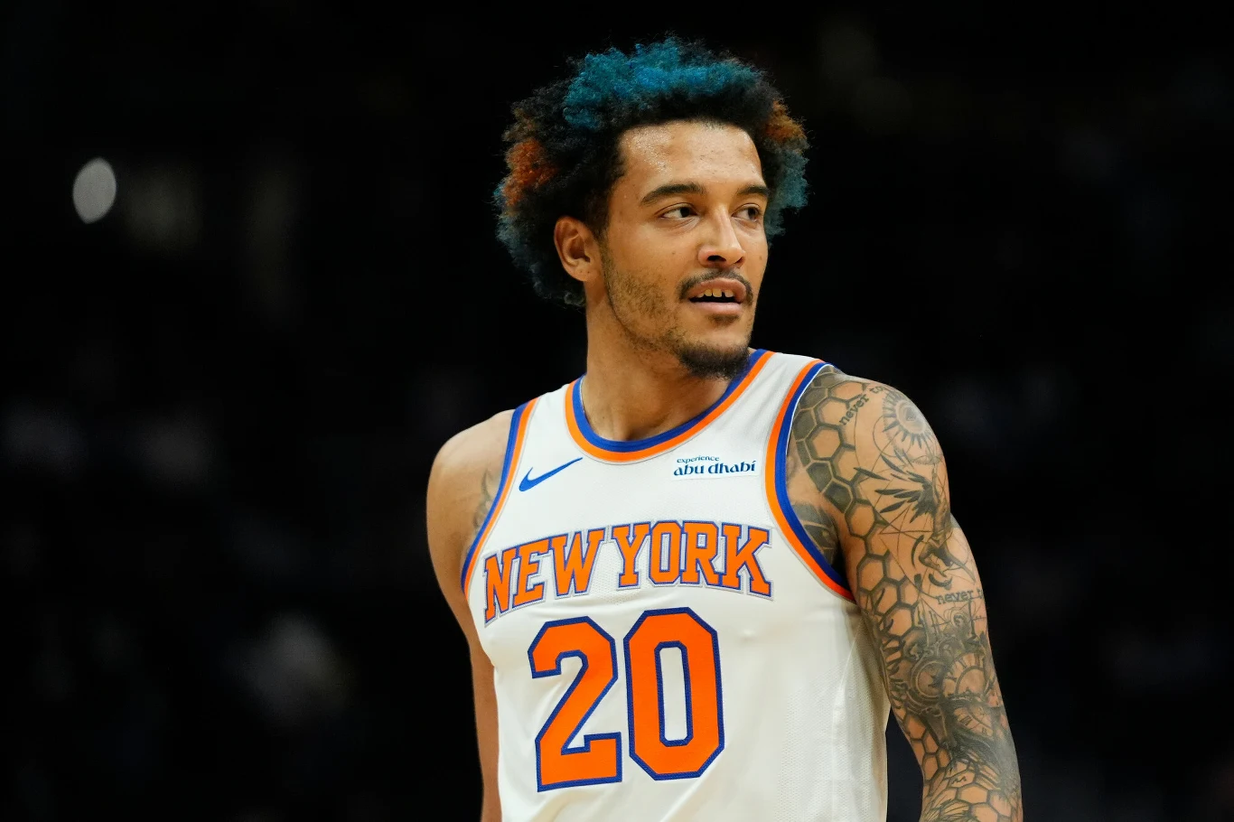 Koszykarz w białym stroju New York Knicks z numerem 20, z tatuażami na ramieniu i niebiesko-pomarańczowymi włosami, patrzy w bok podczas meczu na boisku.