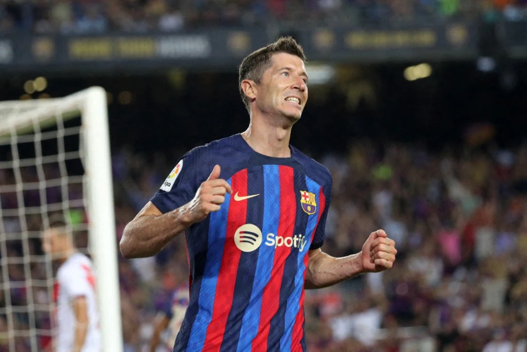 Piłkarz w koszulce FC Barcelony z charakterystycznymi granatowo-czerwonymi pasami i logo Spotify świętuje sukces na boisku, stojąc przed bramką z zaciśniętymi pięściami i wyraźną radością na twarzy.