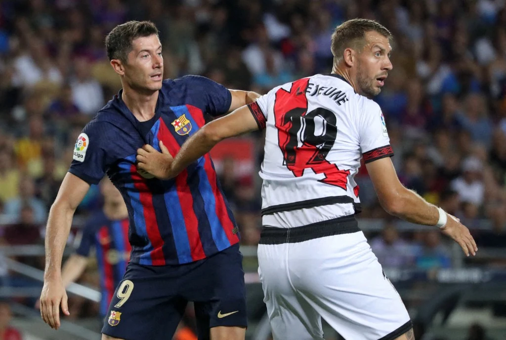 Dwóch piłkarzy rywalizuje o piłkę podczas meczu – jeden w stroju FC Barcelony, drugi w biało-czerwono-czarnym stroju przeciwników; obaj są skupieni i zaangażowani w walkę o pozycję.