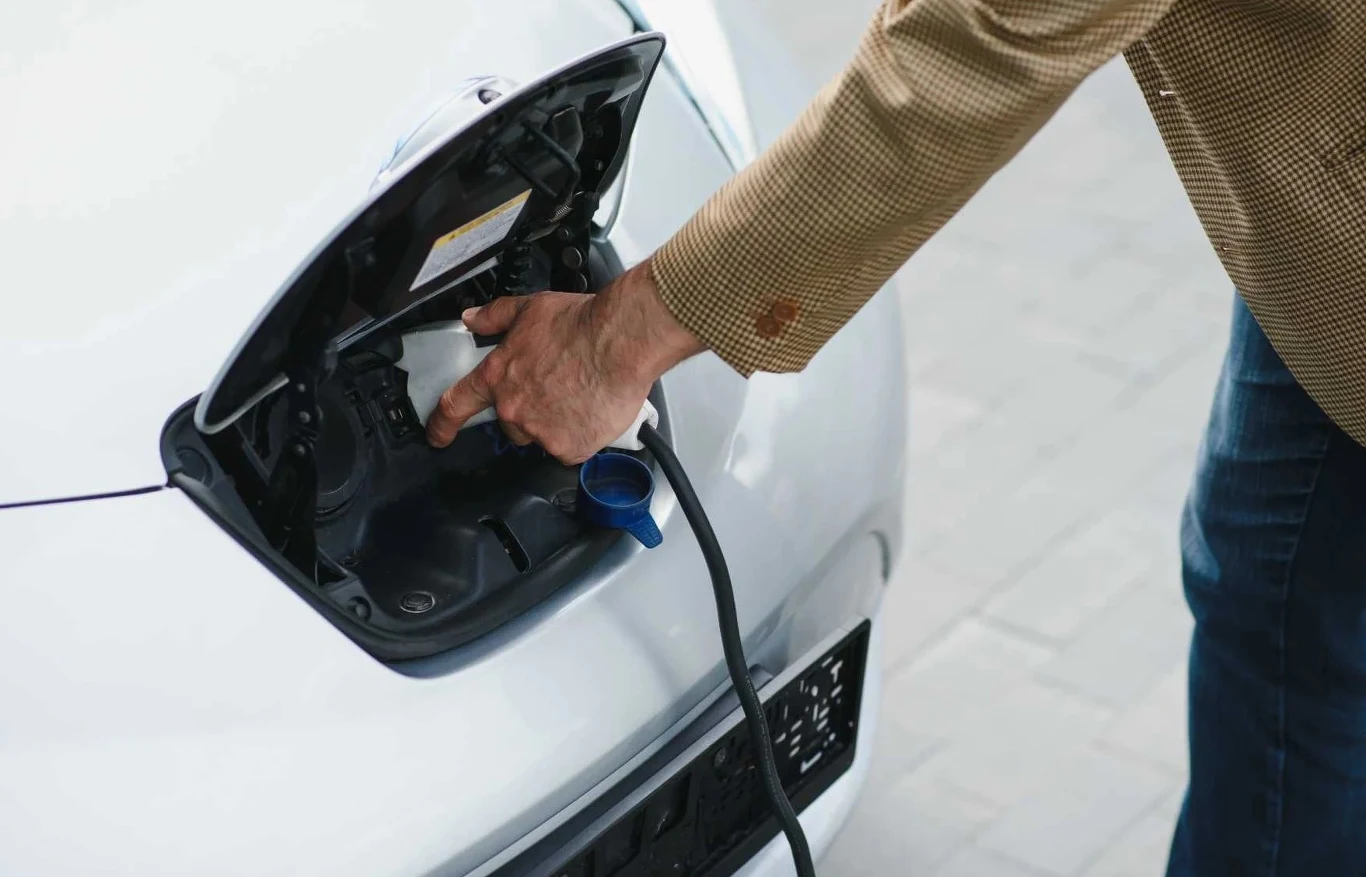 mężczyzna podłącza kabel do ładowania elektrycznego samochodu, otwierając złącze ładowania z przodu pojazdu
