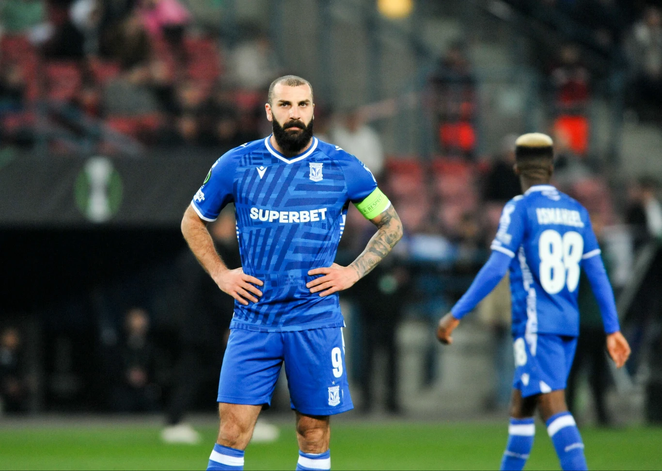 Mikael Ishak w niebieskim stroju z opaską kapitana, obok zawodnik z nr 88, tle trybuny z publicznością