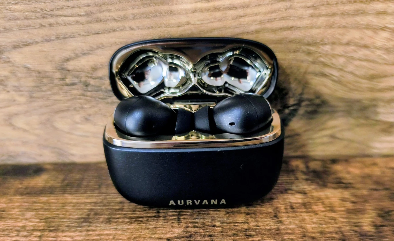 czarne bezprzewodowe słuchawki douszne umieszczone w otwartym etui ładującym z połyskującym wnętrzem, logo marki AURVANA widoczne na przodzie etui, całość ustawiona na drewnianej powierzchni