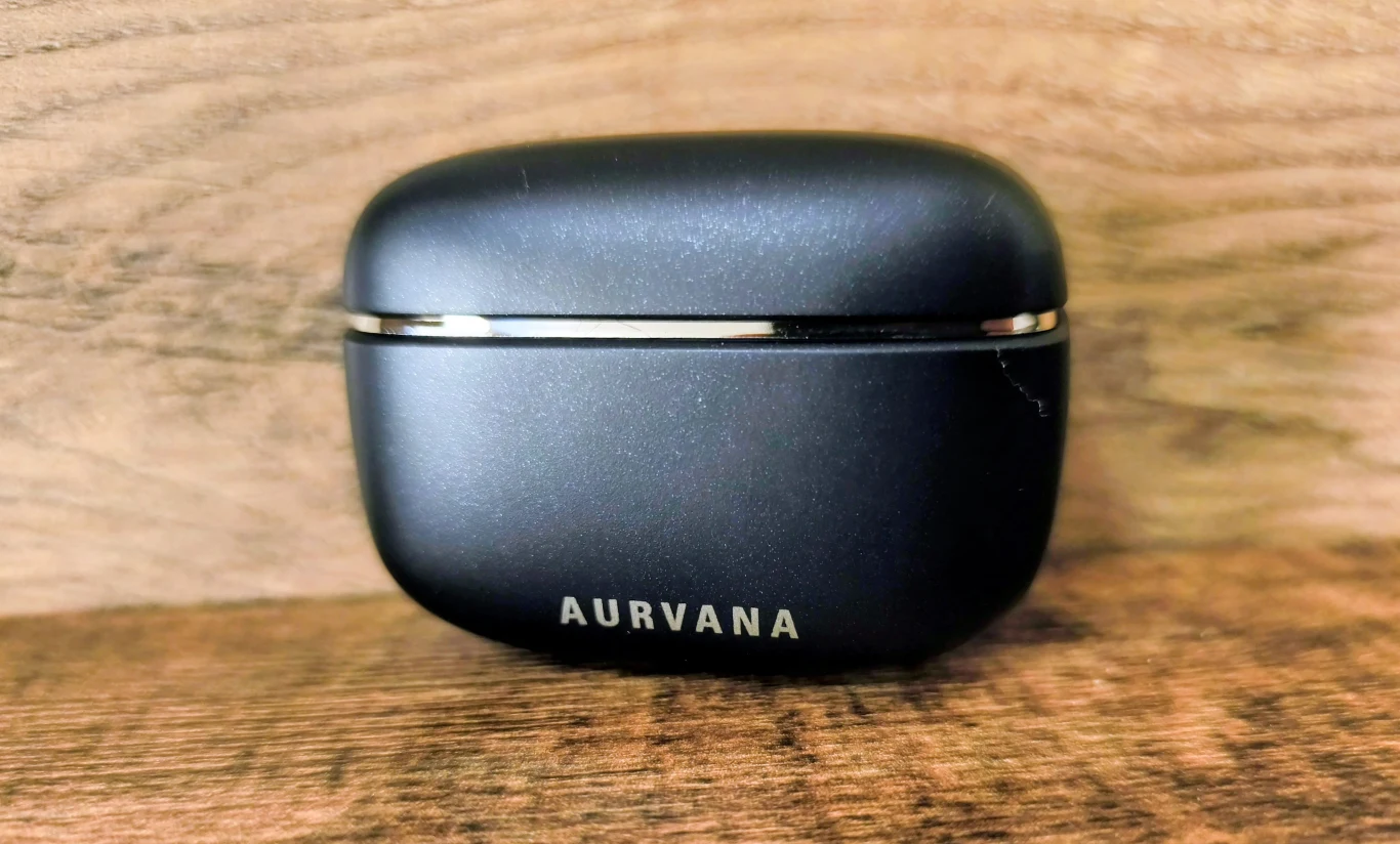 czarne, matowe etui na słuchawki bezprzewodowe z napisem AURVANA na przodzie, ustawione na drewnianej powierzchni na tle jasnego drewna