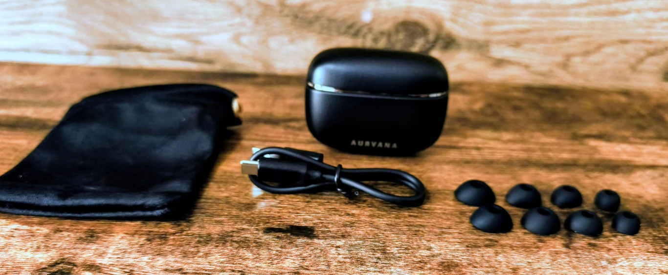 Czarny futerał na słuchawki, etui słuchawek Audvana, krótki kabel USB oraz zestaw silikonowych końcówek dousznych w różnych rozmiarach ułożone na drewnianej powierzchni.
