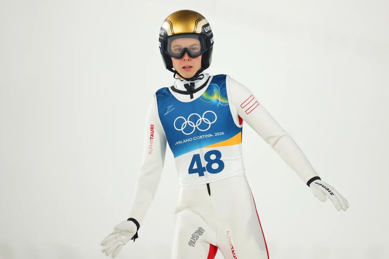 skoczek narciarski w kombinezonie i kasku lądujący na śniegu podczas zimowych igrzysk olimpijskich, na piersi numer startowy 48 oraz olimpijskie logo