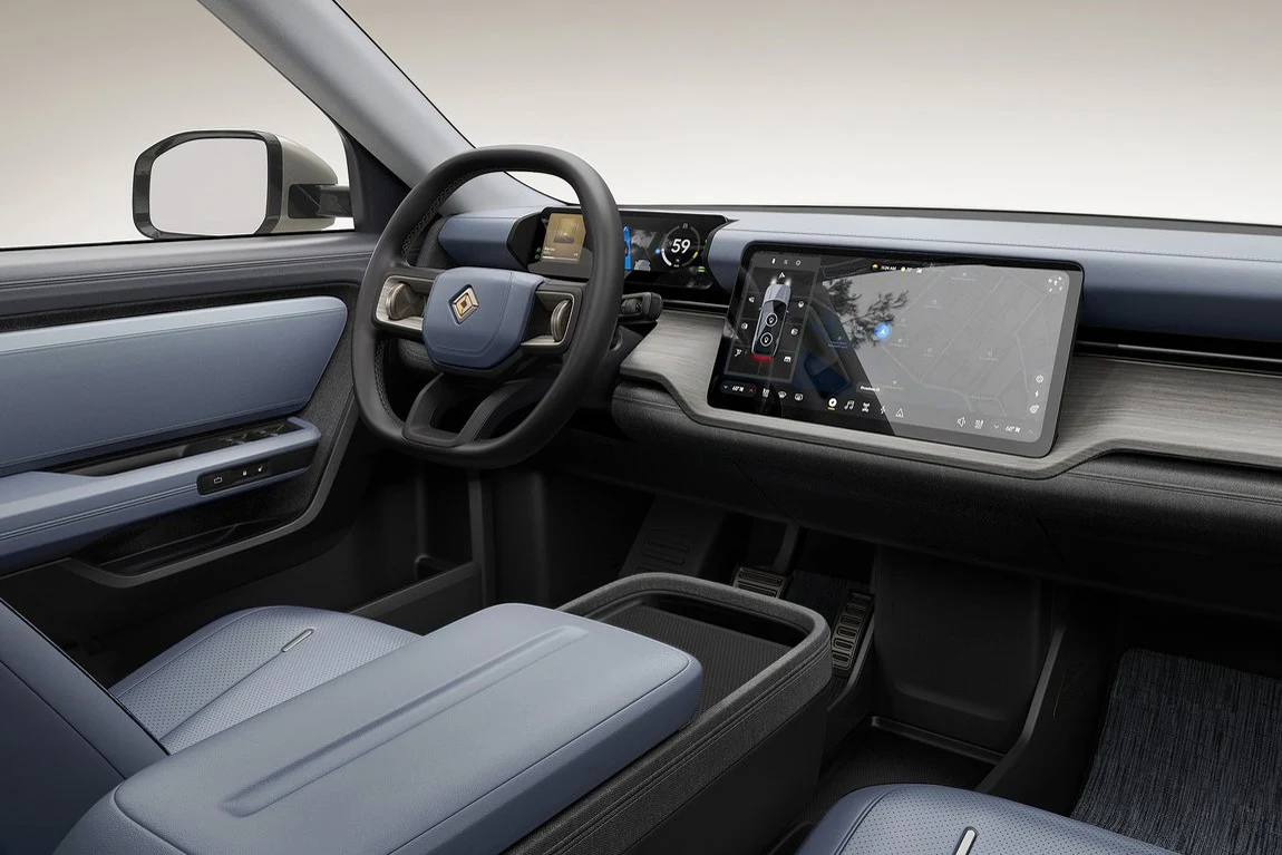 nowoczesne wnętrze samochodu z jasnoniebieskimi fotelami, dużą kierownicą, cyfrowym zestawem wskaźników oraz szerokim, poziomym ekranem dotykowym na konsoli środkowej; minimalistyczny design z dominacją geometrycznych kształtów i stonowanej kolorystyki