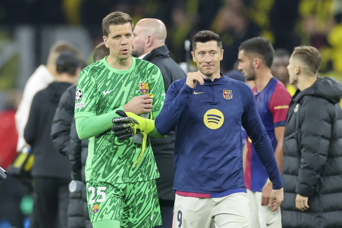 Wojciech Szczęsny w zielonym stroju i Robert Lewandowski w trykocie Barcelony na murawie, obok inni piłkarze.