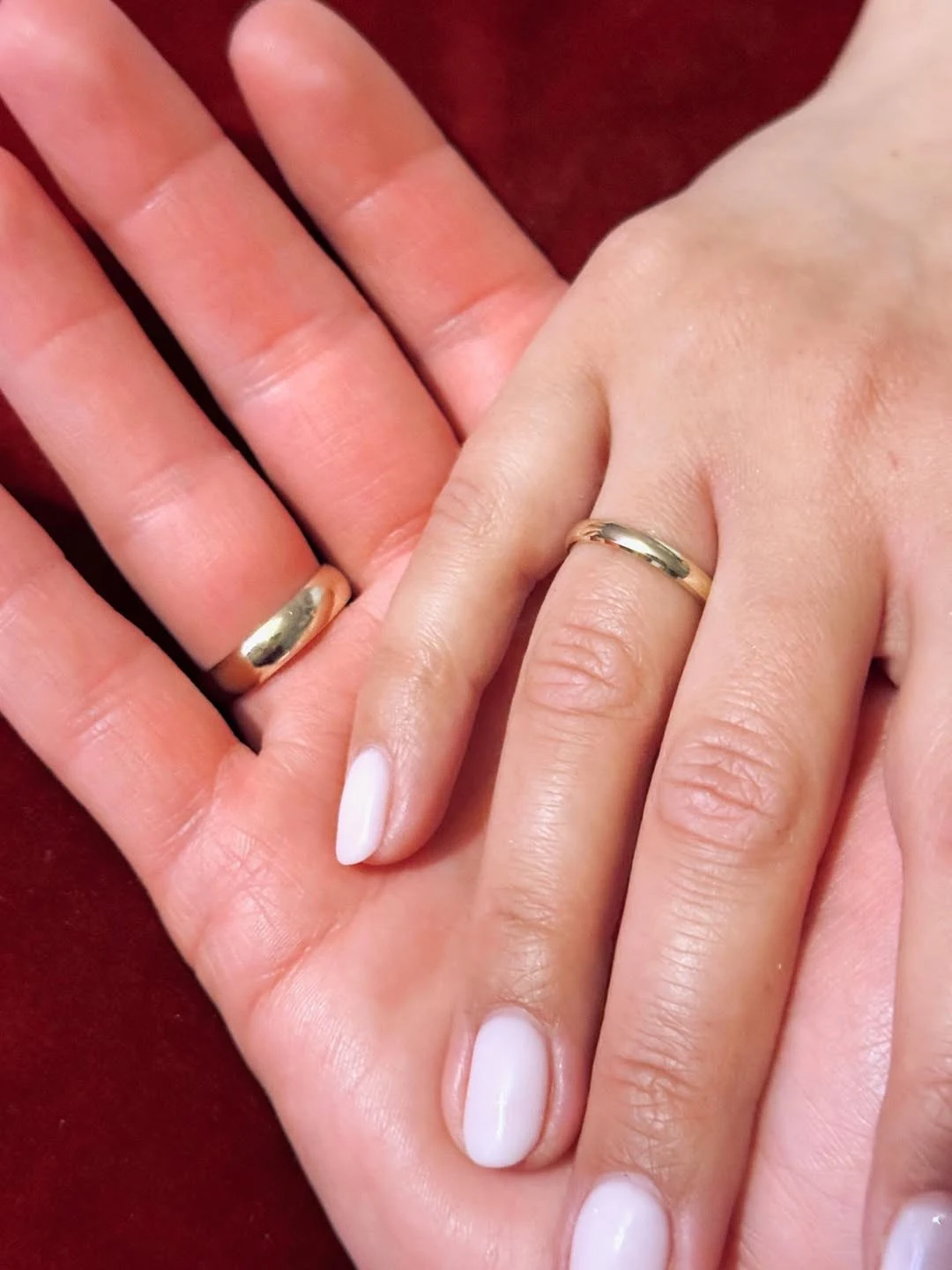 dwie dłonie z obrączkami leżące na sobie na tle bordowej tkaniny, wskazujące na związek lub małżeństwo