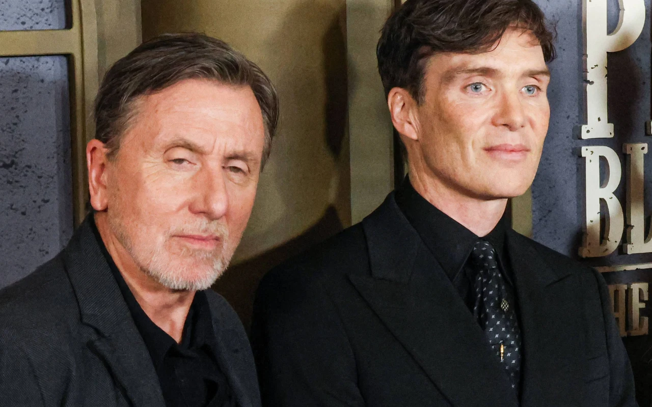 Tim Roth i Cillian Murphy Tim Roth i Cillian Murphy pozują na tle ściany z logo "Peaky Blinders", obaj mają na sobie ciemne garnitury.