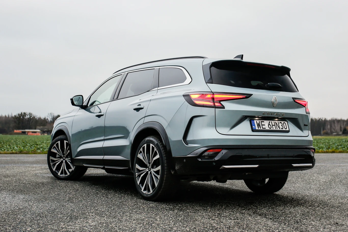 srebrny SUV z przyciemnianymi szybami i charakterystycznym tylnym oświetleniem LED, stojący na asfaltowej drodze na tle pola i pochmurnego nieba