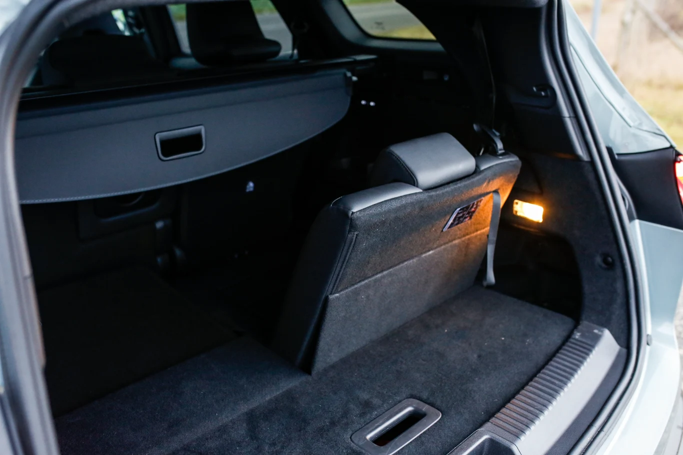 bagażnik samochodu z częściowo złożonym tylnym siedzeniem, widoczne czarne tapicerowane wnętrze i osłona bagażowa oraz delikatne oświetlenie wnętrza po prawej stronie
