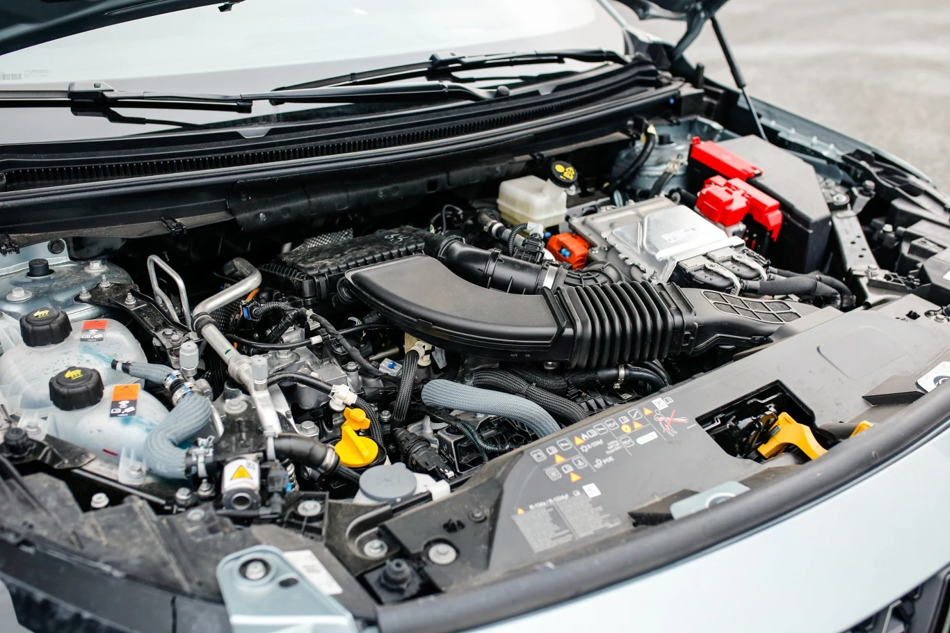 silnik samochodu z widocznymi elementami takimi jak akumulator, filtr powietrza, przewody oraz zbiorniki płynów technicznych