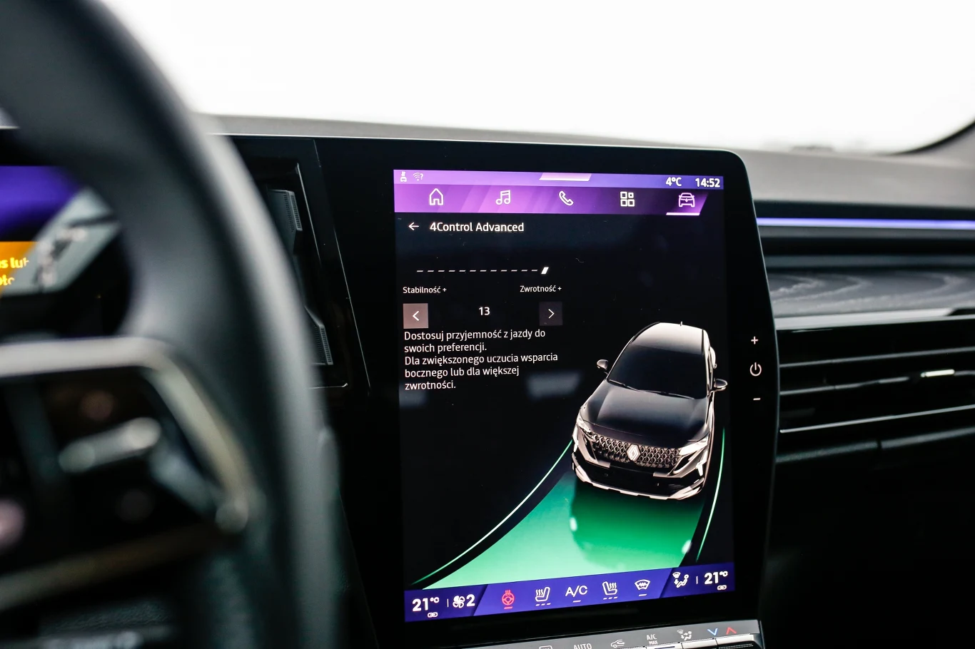 Duży ekran dotykowy w samochodzie wyświetlający interfejs systemu multimedialnego oraz wizualizację pojazdu z aktywnymi ustawieniami wspomagania jazdy i klimatyzacji, z widocznym fragmentem kierownicy po lewej stronie.