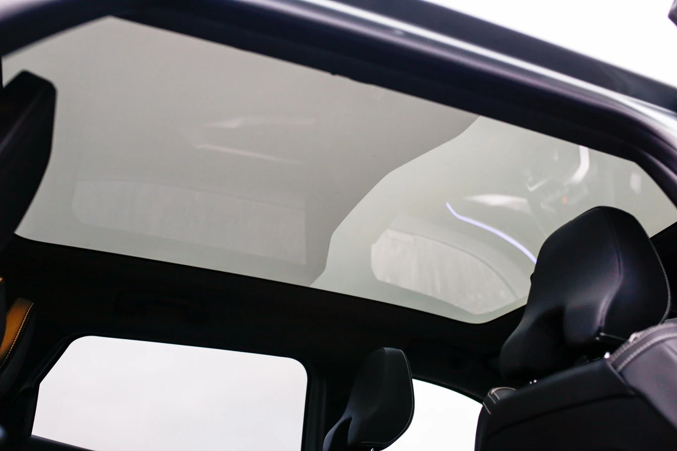 przestronne wnętrze samochodu wyposażone w duży, panoramiczny dach szklany oraz nowoczesne, czarne fotele