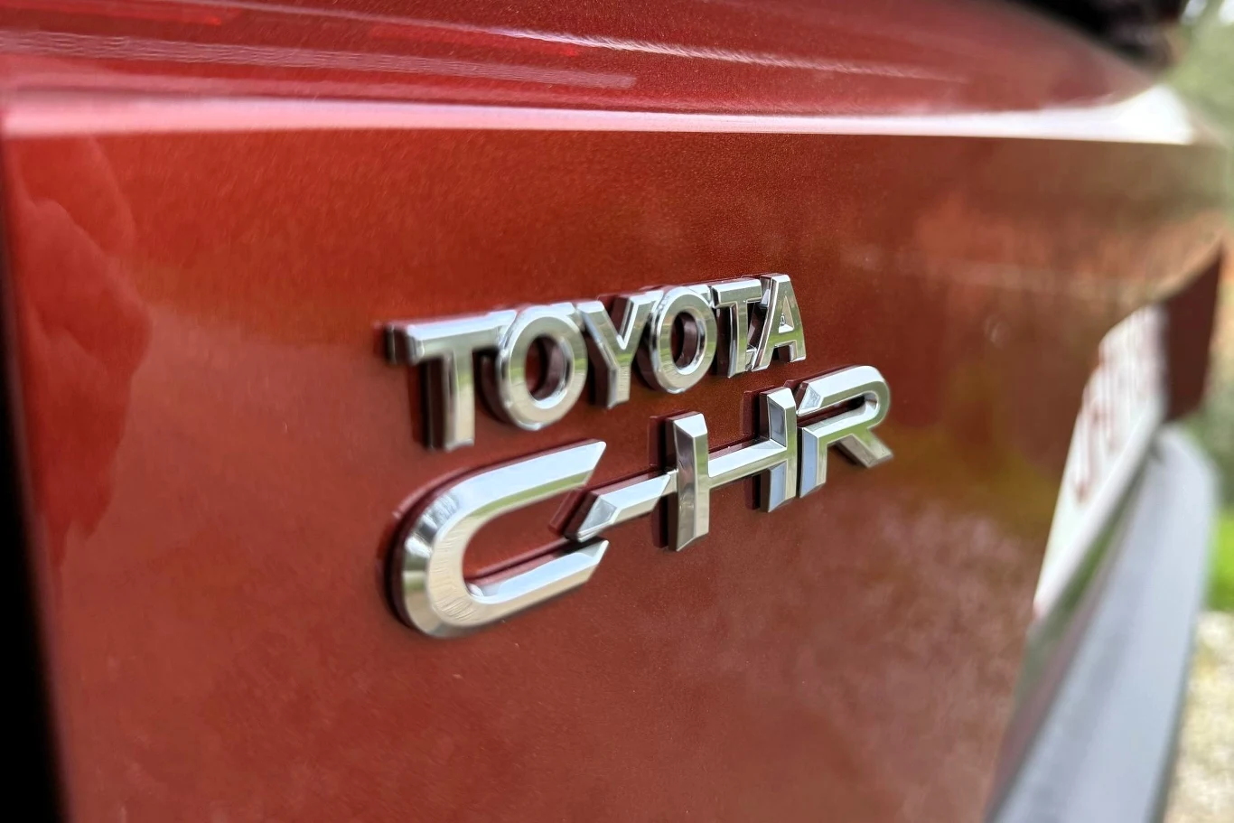 chromowany emblemat Toyota C-HR na bordowym lakierze samochodu