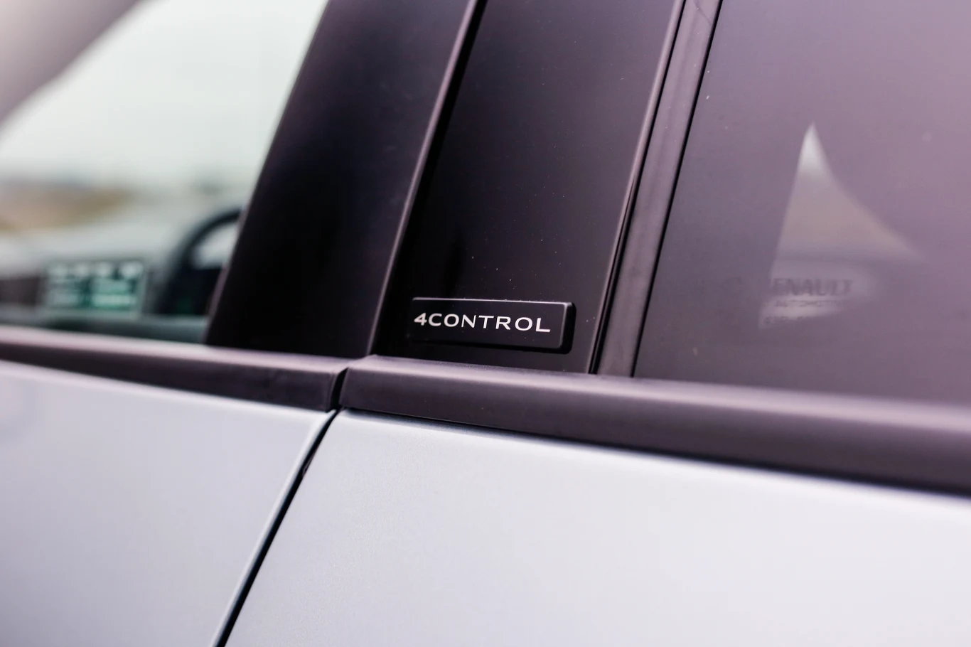 czarny emblemat z napisem „4CONTROL” umieszczony na słupku między szybami samochodu o jasnej karoserii
