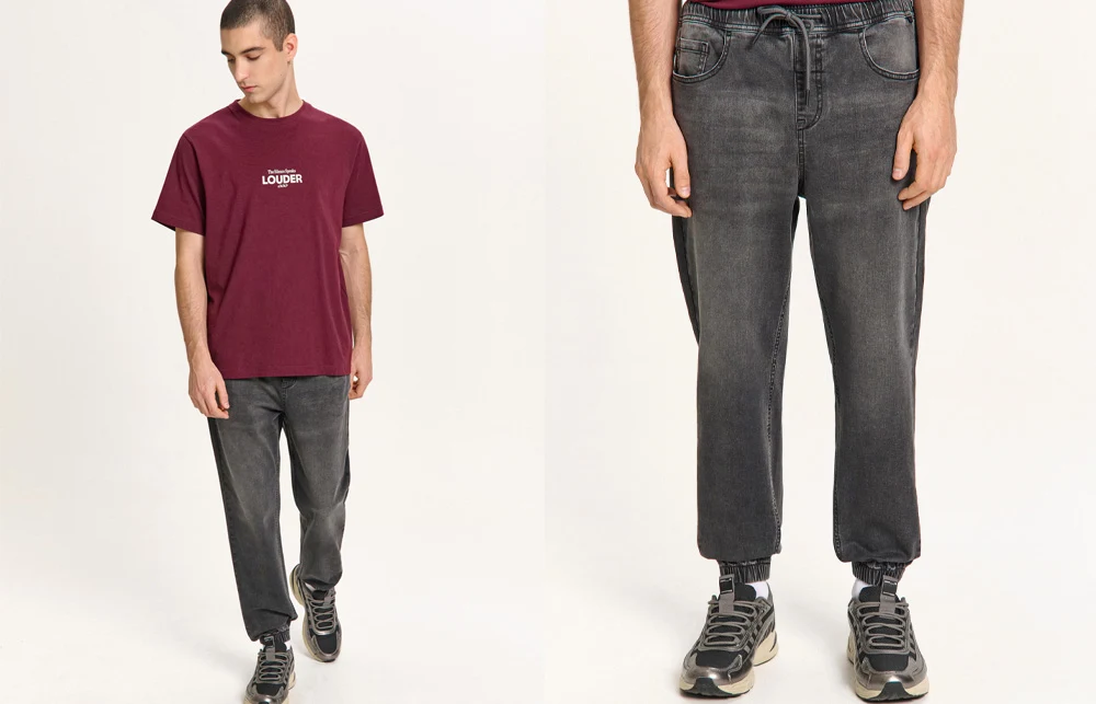 mężczyzna ubrany w bordowy t-shirt z białym napisem oraz luźne czarne jeansy i sportowe buty, prezentuje swobodny, codzienny styl