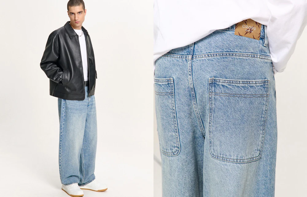 Mężczyzna ubrany w białą koszulkę, czarną skórzaną kurtkę i szerokie, jasnoniebieskie jeansy z dużymi kwadratowymi kieszeniami z tyłu, białe sneakersy dopełniają stylizację.