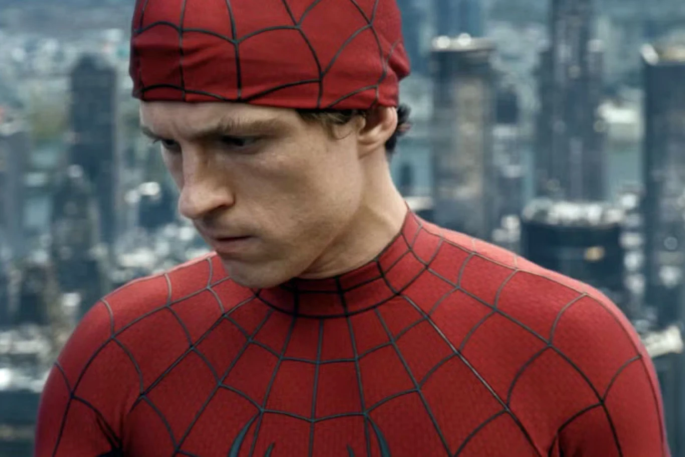Mężczyzna w kostiumie Spider-Mana z poważnym wyrazem twarzy na tle panoramy miasta z wieżowcami w tle.