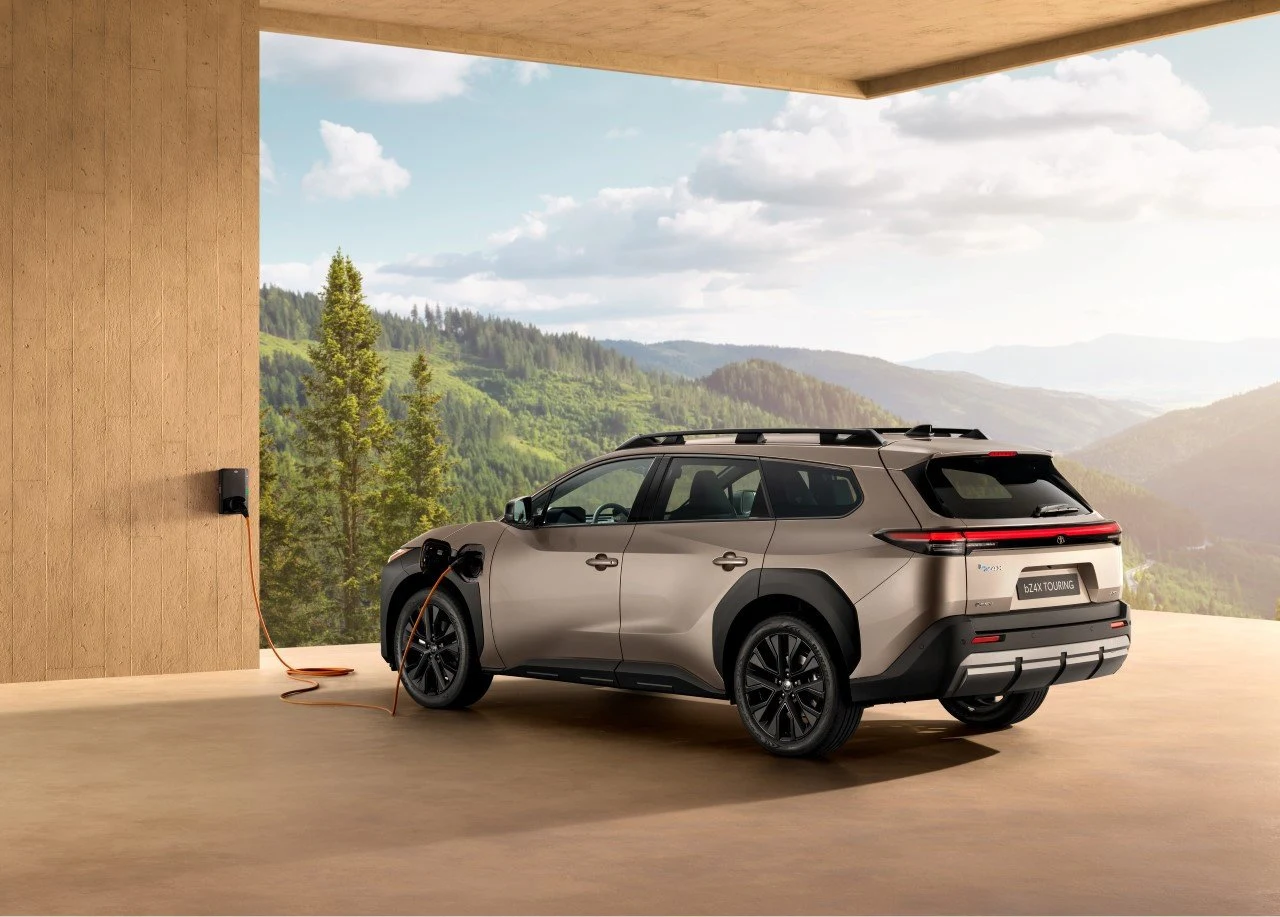 Nowoczesny samochód elektryczny ładowany przy domowej stacji ładowania, ustawiony na tarasie z widokiem na górski krajobraz i otaczające lasy.