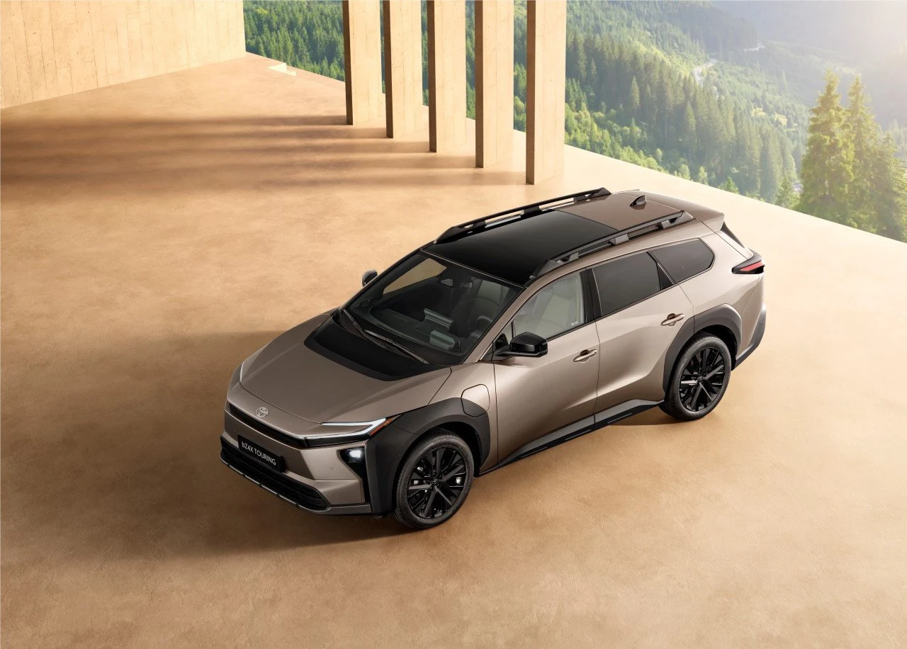 nowoczesny, duży SUV w kolorze szampańskim z czarnym dachem i relingami, stojący na jasnej posadzce przy filarach budynku, w tle zielony krajobraz górski