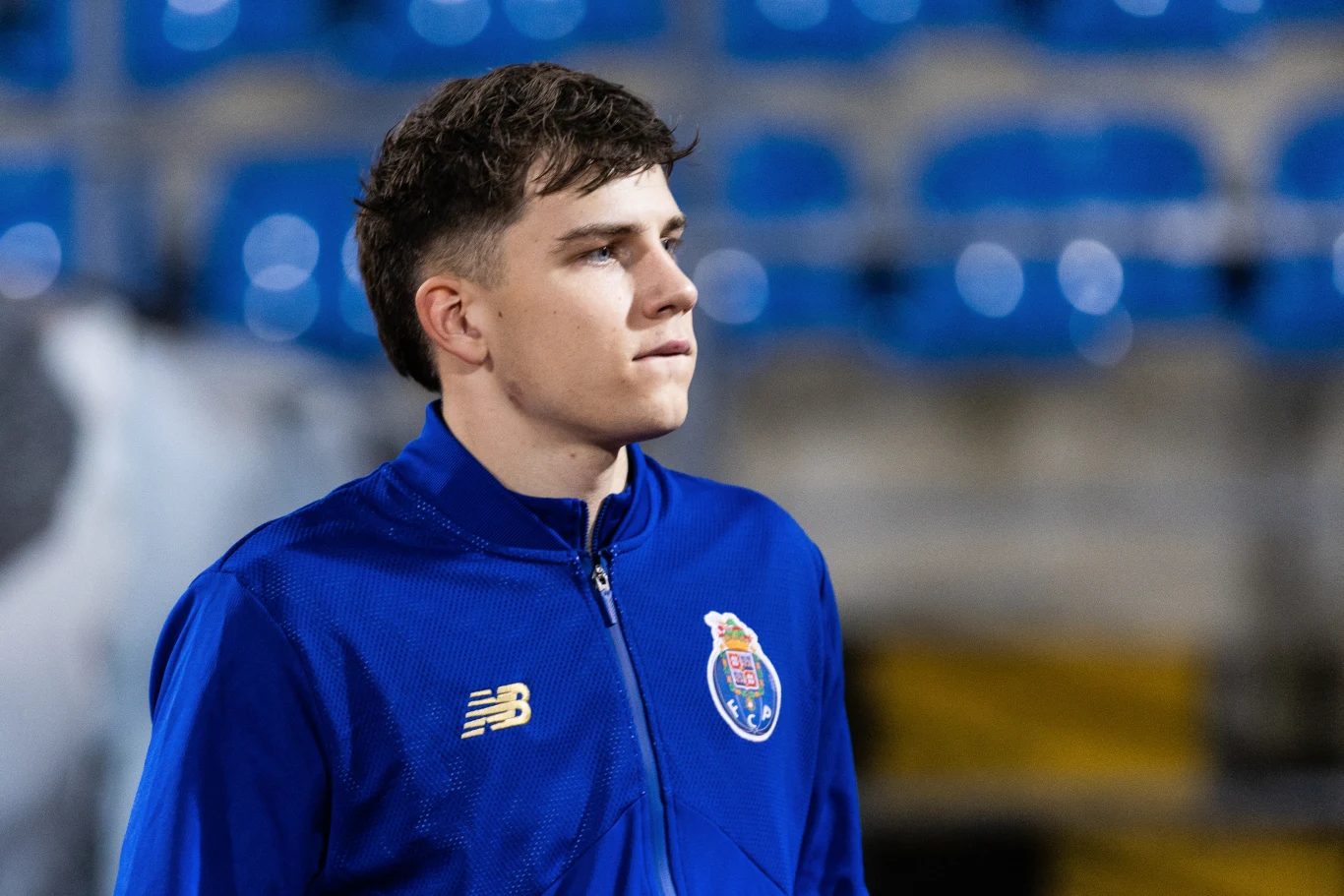 młody mężczyzna w niebieskiej sportowej kurtce z herbem klubu piłkarskiego FC Porto, patrzący w dal na tle pustych niebieskich trybun stadionu