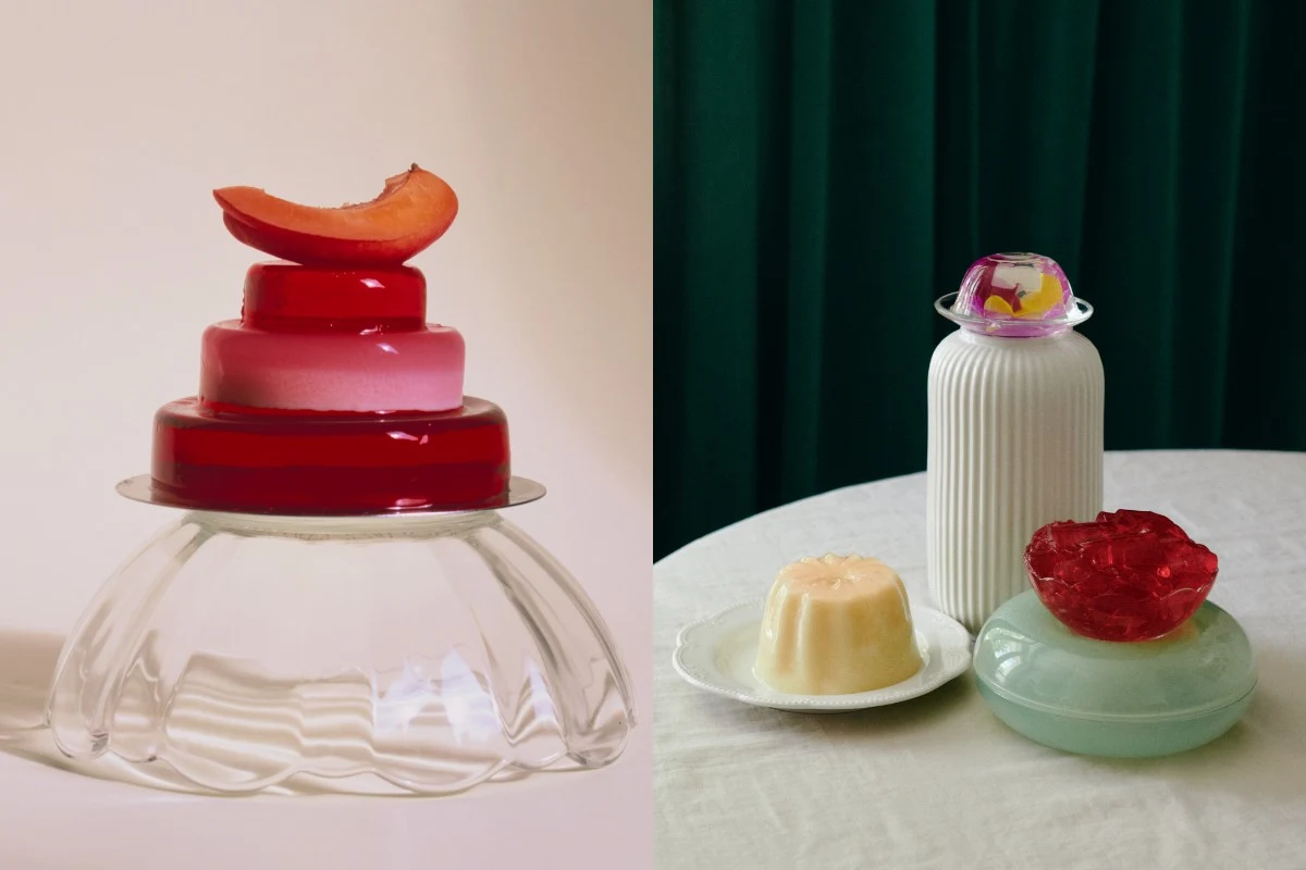 Artystycznie ułożone desery z galarety w intensywnych kolorach i owocami, ustawione na szklanych i ceramicznych naczyniach oraz białej butelce na tle zielonej zasłony; kompozycja podkreślająca kontrast form i barw.