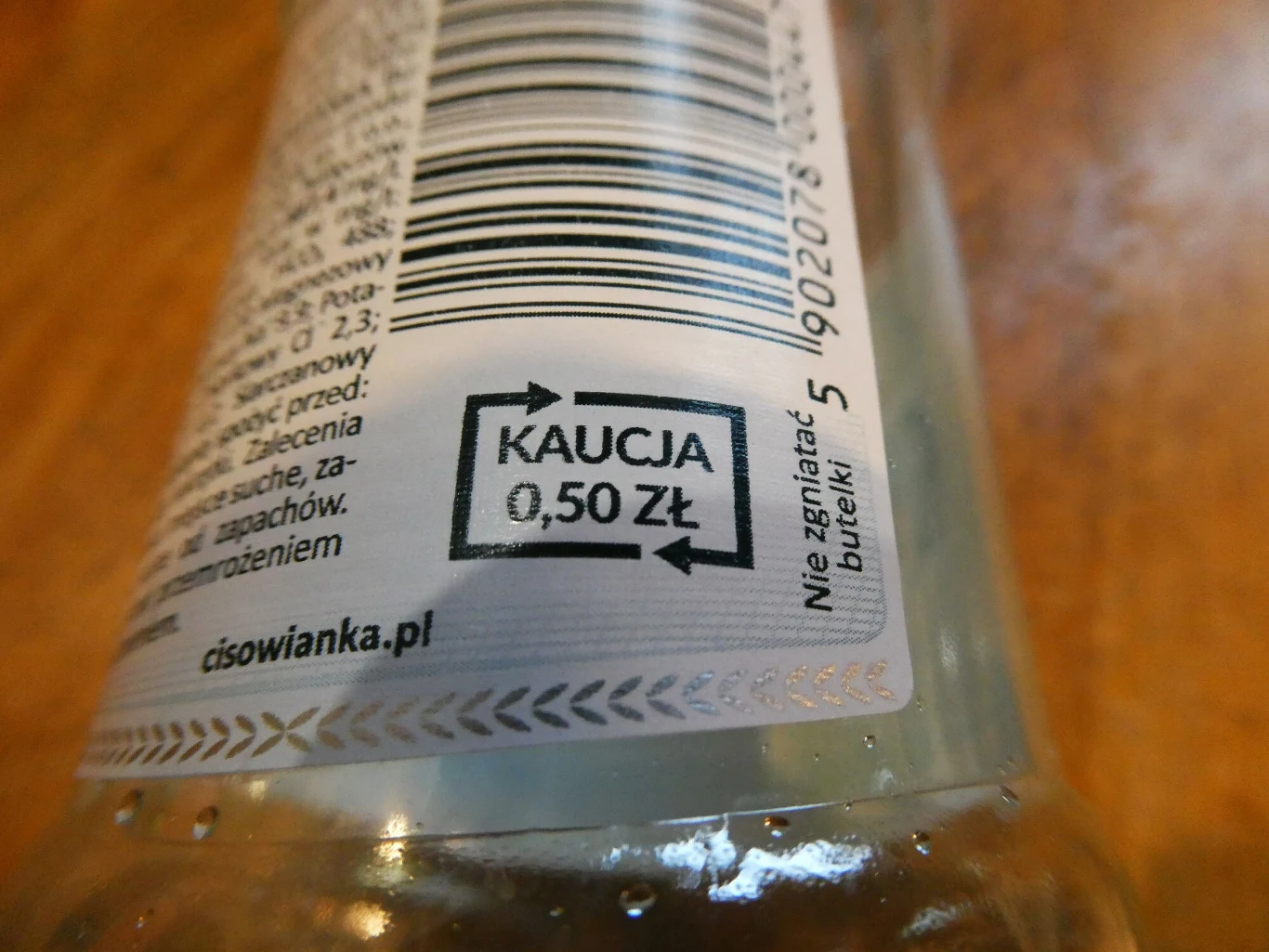 Etykieta butelki z kodem kreskowym, oznaczeniem kaucji w wysokości 0,50 zł oraz ostrzeżeniem 'Nie zgnie­taj butelki'.