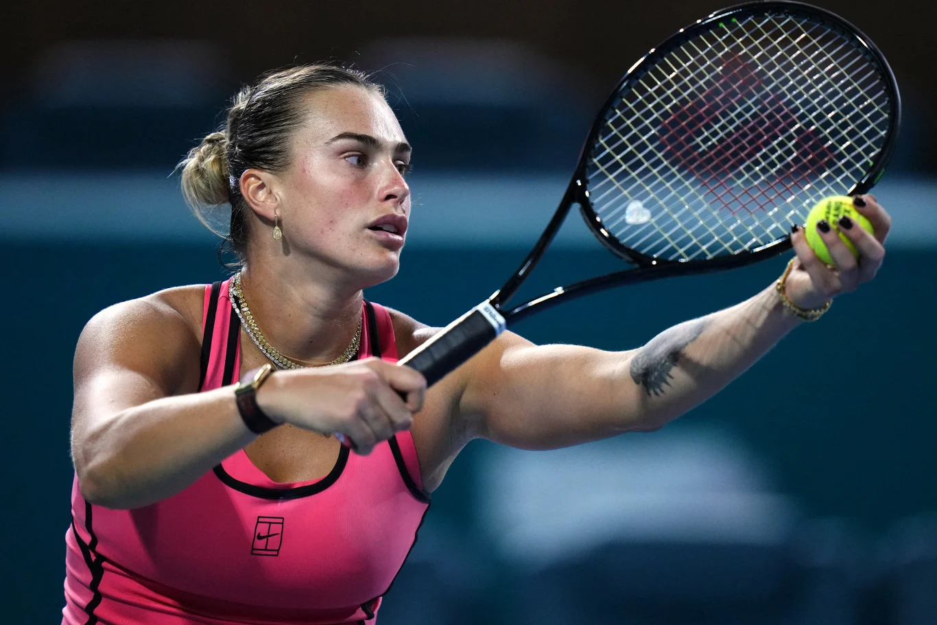 tenisistka w różowej koszulce skupiona podczas serwowania, trzyma rakietę i żółtą piłkę tenisową w gotowości do rozpoczęcia wymiany