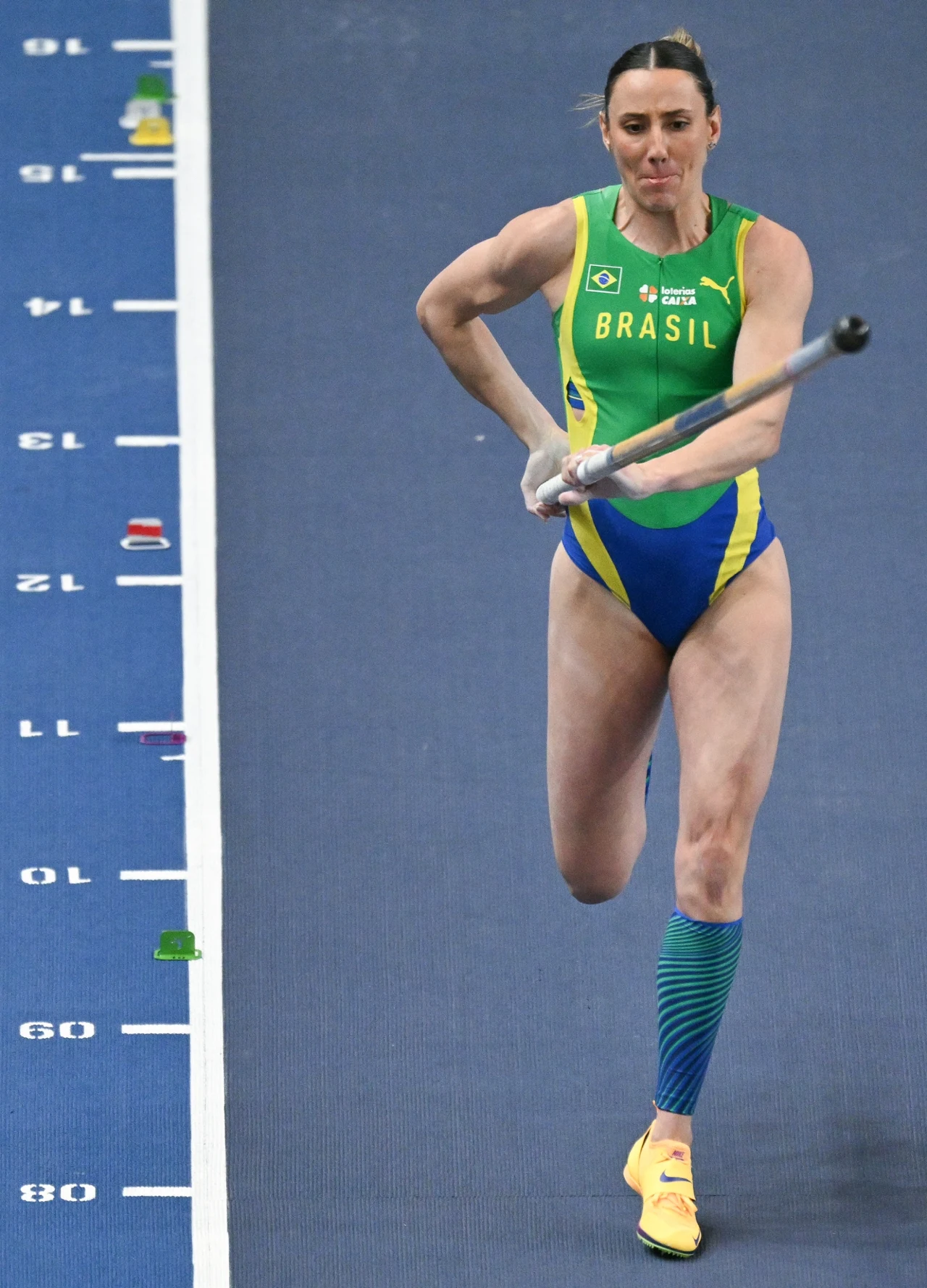 lekkoatletka z Brazylii w stroju sportowym biegnie z tyczką po bieżni w trakcie zawodów lekkoatletycznych