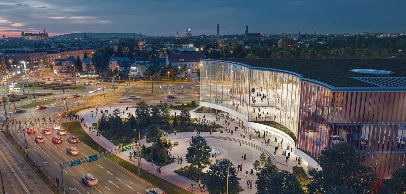 nowoczesny budynek z przeszkloną fasadą otoczony zielenią, oświetlony w wieczornym świetle, z wieloma osobami wchodzącymi i opuszczającymi obiekt, położony przy ruchliwym rondzie z widokiem na panoramę miasta w tle
