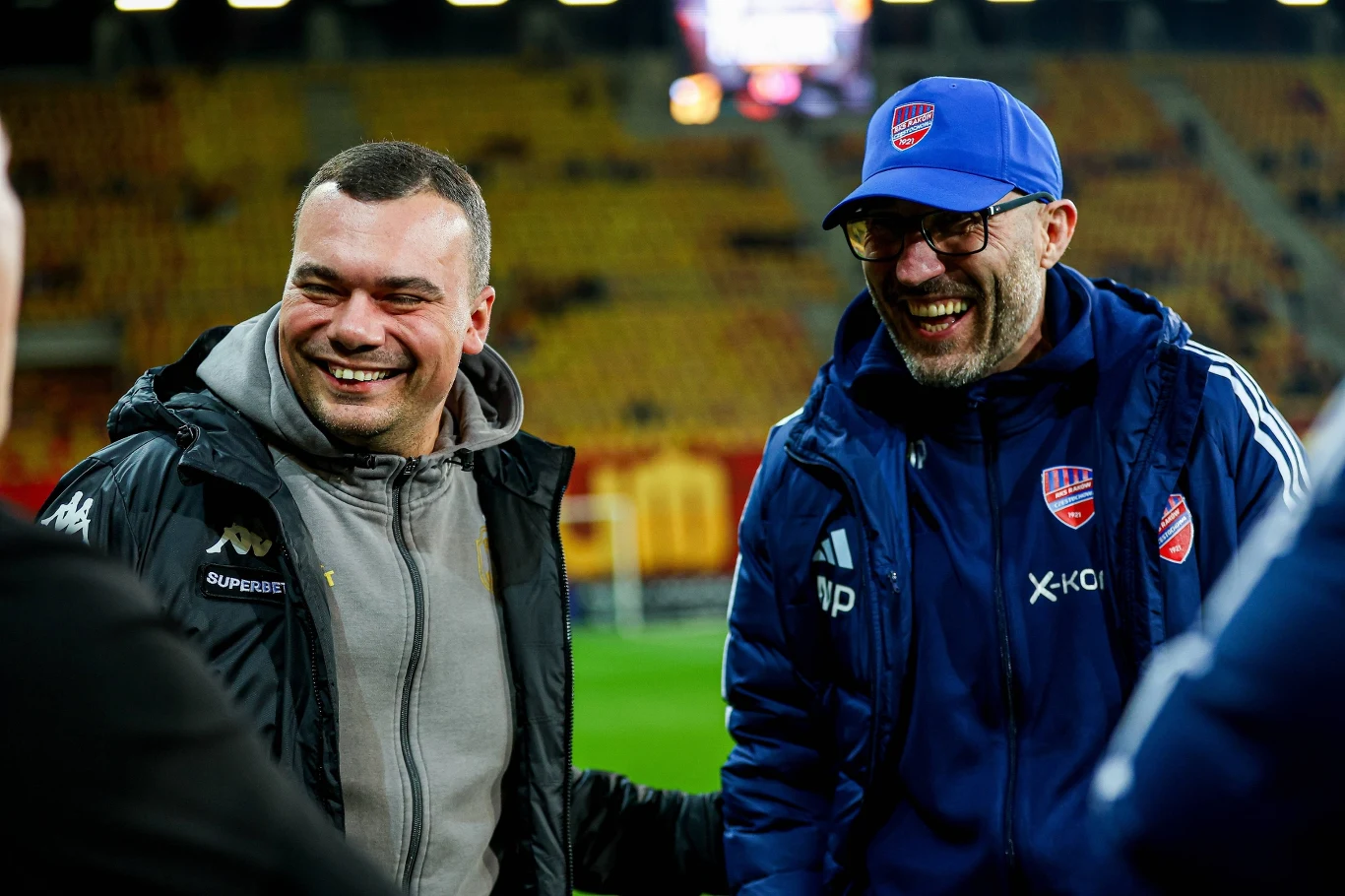Adrian Siemieniec i Marek Papszun rozmawiają na stadionie, w klubowych strojach sportowych.